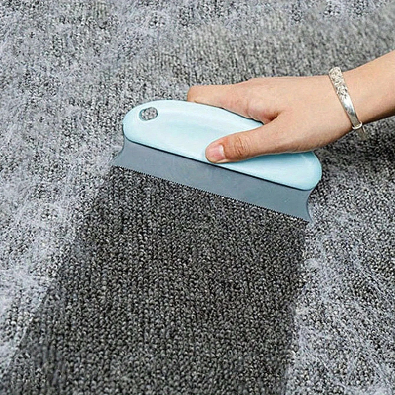 Handheld light blue brush removing fuzz from gray carpet pile