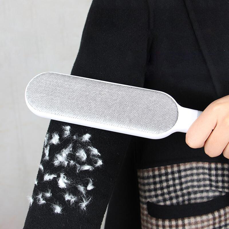 Reusable pet hair remover brush with gray pad removing white fur from black fabric